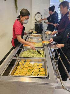 厨房スタッフが学生に料理を提供中