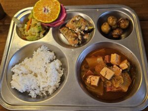 ご飯、野菜炒め、チヂミ、豆腐チゲ、フルーツが盛られた夕食