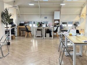 窓際に複数の机と椅子が並ぶ白を基調としたオフィス