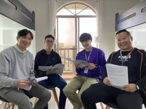 教材を手にした講師と生徒が椅子に座って笑顔を見せる様子