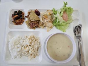 天ぷら、キムチ、サラダ、クラムチャウダー、ご飯が盛られた朝食