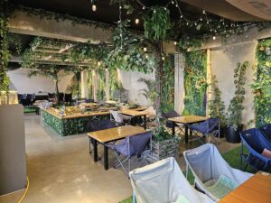 植物と照明で飾られ、アウトドアチェアが並ぶ校舎内のレストラン