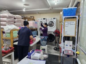 シーツ類が棚に並べられ、2人のスタッフが作業しているランドリー