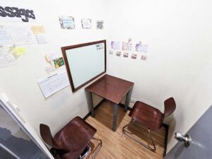 ホワイトボードと机、L字に配置された椅子のあるマンツーマン教室