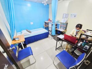 ベッドと椅子が設置された看護室と机に座る看護師