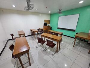 長机、天井扇風機、ホワイトボードが設置された広めのグループ教室