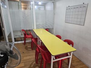 2台のテーブルと椅子が並び扇風機があるグループ教室