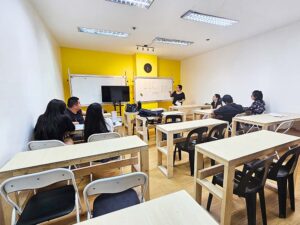2人掛けの机が並ぶ大きなグループ教室で授業に参加する生徒たち