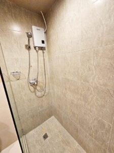 シャワーと蛇口、石鹸トレイのあるタイル張りのシャワーエリア