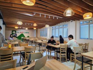 木で装飾された天井、暖色ライト、木製テーブルが並ぶダイニング
