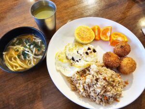 炒飯、コロッケ、卵料理に、スープヌードルとオレンジが添えられた朝食