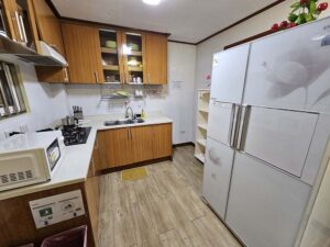 大きな冷蔵庫、電子レンジ、コンロ、シンクがある共用キッチン