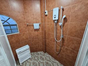 温水器とシャワー、小物ラックが備わった共用シャワールーム