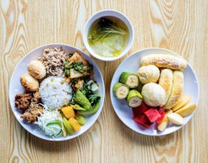 チキン、ゆで卵、野菜炒め、ライス、スープ、パンと果物が並ぶプレート