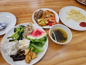 チキンアドボ、トッポギ、3種の野菜炒め、スープ、フルーツが並ぶ昼食チキンアドボ、トッポギ、3種の野菜炒め、スープ、フルーツが並ぶ昼食