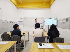モニターを指さすネイティブ講師の説明に聞き入る3人の生徒