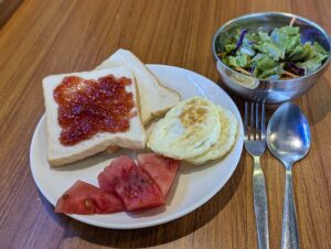 トーストと目玉焼き、スイカが盛られた皿とサラダが並ぶ朝食