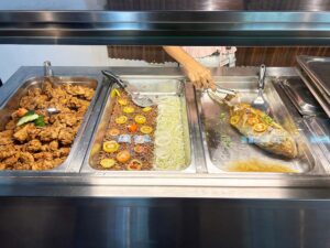 キッチンスタッフが焼き魚を取り分けている主菜コーナー