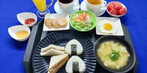 おにぎり、サンドイッチ、味噌汁、サラダ、果物、ドリンクが並ぶ朝食