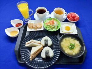 おにぎり、サンドイッチ、味噌汁、サラダ、果物、ドリンクが並ぶ朝食