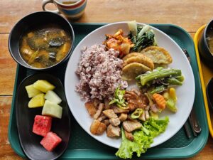 紫米、焼いた豚肉、炒め野菜、揚げ物、果物などが盛られた昼食