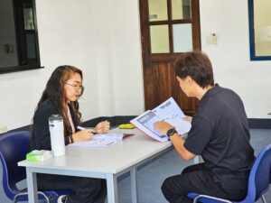 体験授業でテキストを音読する生徒と、耳を傾けている講師