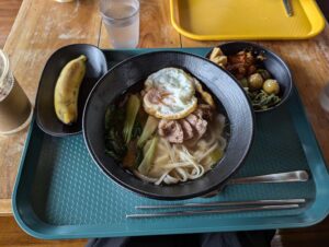 目玉焼きと豚肉のヌードル、韓国風副菜、バナナが添えられた昼食