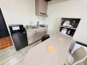 テーブル、電子レンジ、冷蔵庫、シンク、コンロ、食器類が備わったキッチン