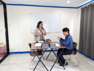 ホワイトボードの前で体験授業の生徒の話に耳を傾ける講師