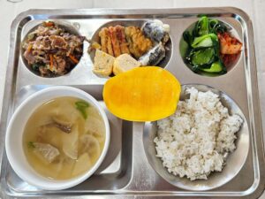 牛肉炒め、卵焼き、揚げ物、スープ、マンゴーが盛られた給食トレイ