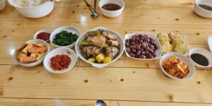 鶏肉の煮物、天ぷら、キムチ、青菜、ぶどうが並ぶ食卓