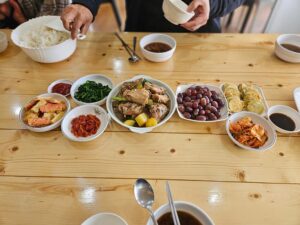 鶏肉の煮物、天ぷら、キムチ、青菜、ぶどうが並ぶ食卓
