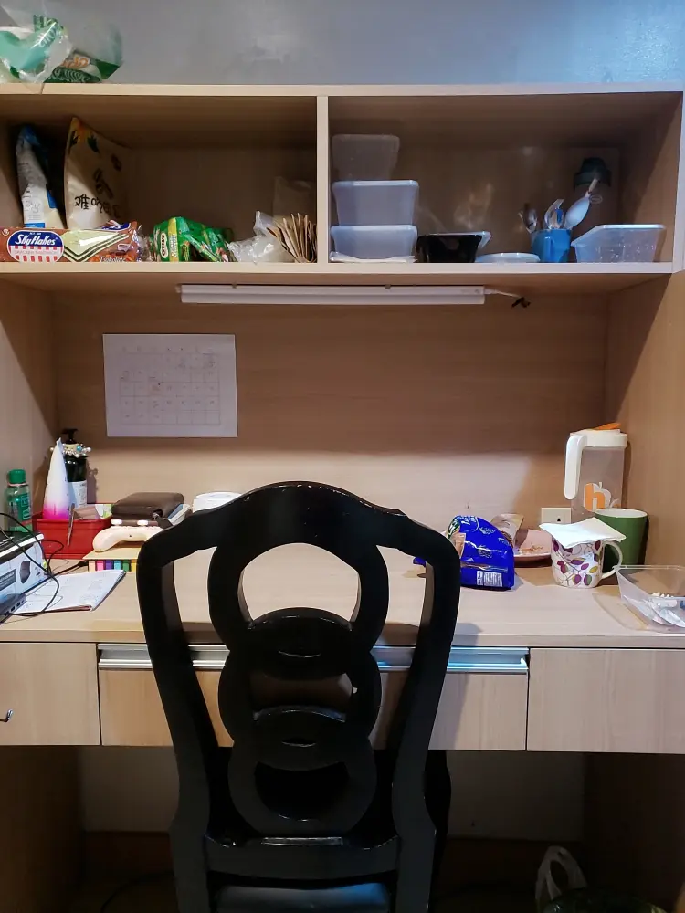 スナック、タッパー、文房具が置かれた学生寮の部屋の机