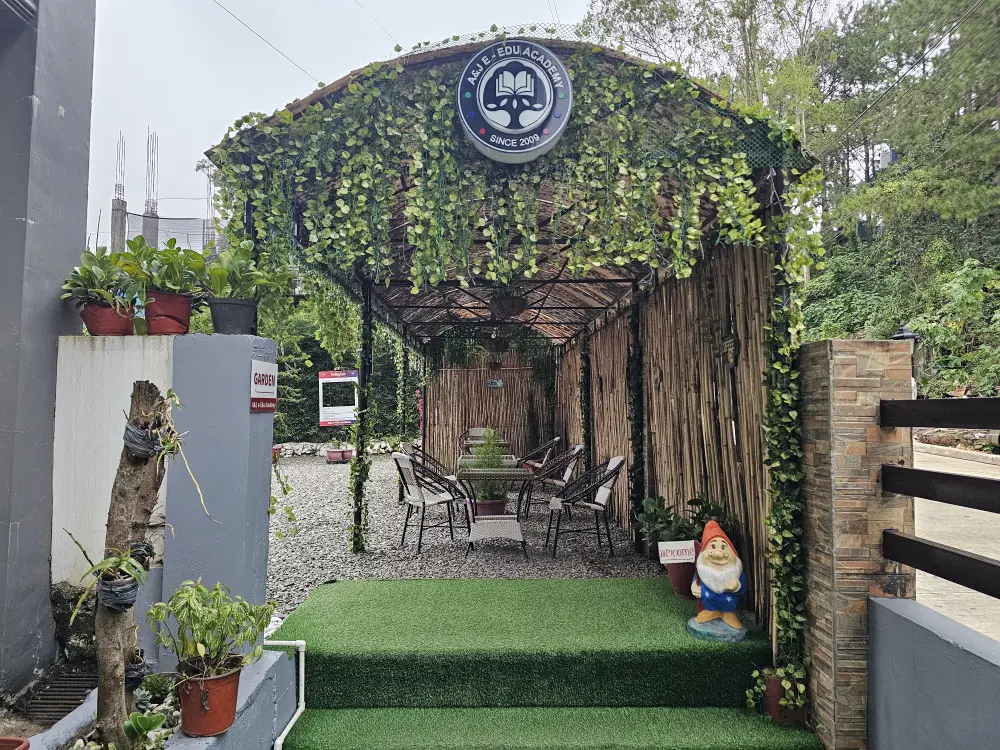 A&Jメインの校門側から見た校庭と屋根付きの屋外学習エリアのテーブルと椅子