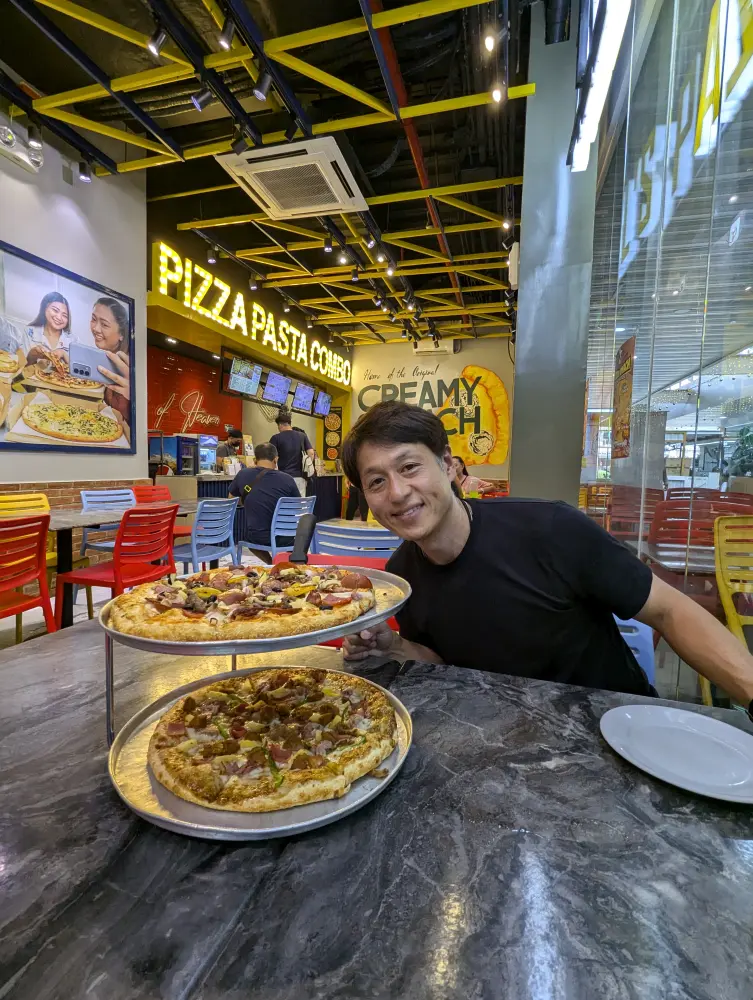 LGガーデンウォーク・マクタンのレストランで2枚のピザを前にして笑顔になる真太郎