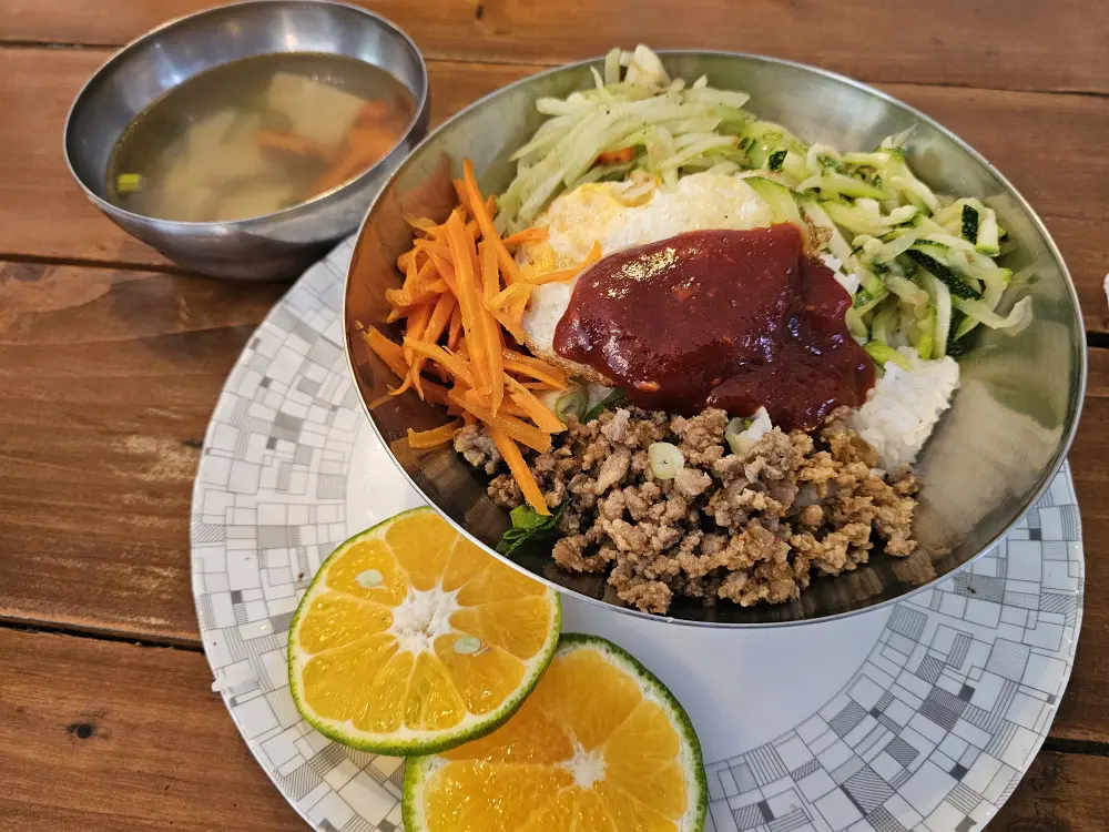 人参、ズッキーニ、ひき肉、卵入りのビビンバにチキンスープ、マンダリンを添えたランチ