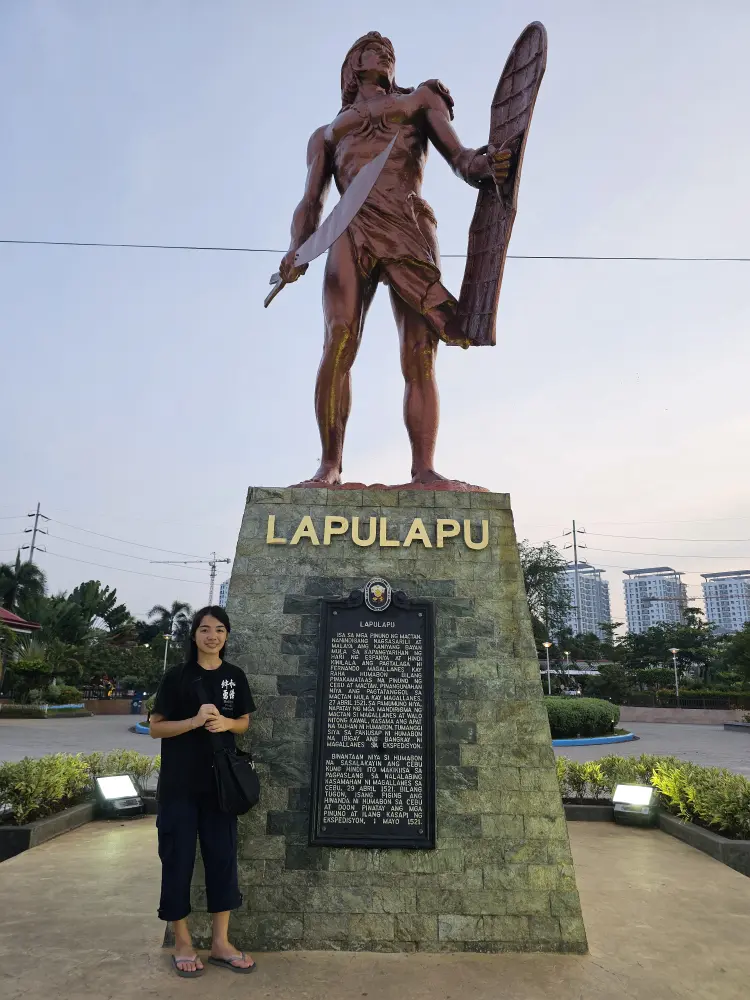 Mactan Shrineでラプラプ像の隣に笑顔で立つGrit留学のジェニー