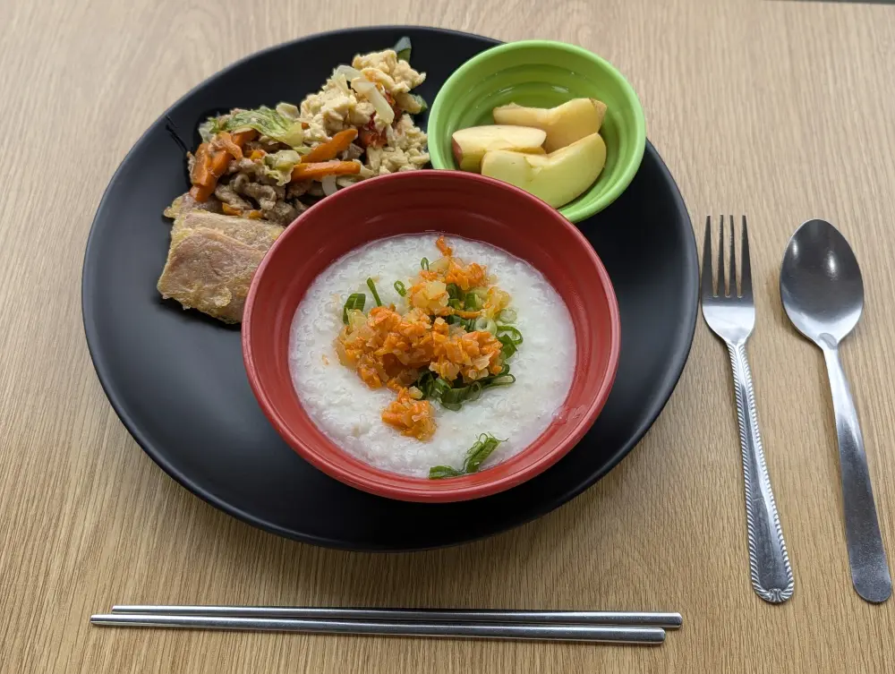 おかゆ、ハム、スクランブルエッグ、りんごのスライスのシンプルな朝食