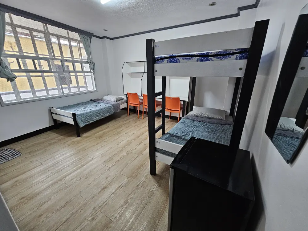 二段ベッドとシングルベッド、3人用勉強机、冷蔵庫が設置された校内寮のトリプルルーム