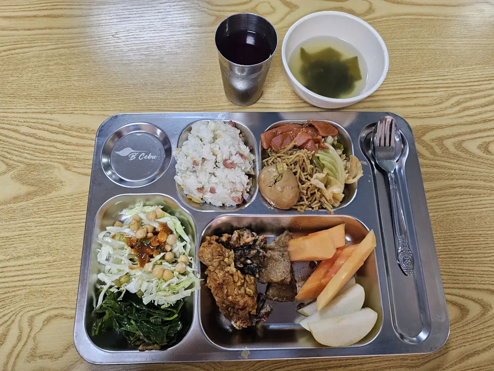 ご飯、チキン、ポークアドボ、焼きそば、サラダ、パパイヤが盛られたビーセブの夕食