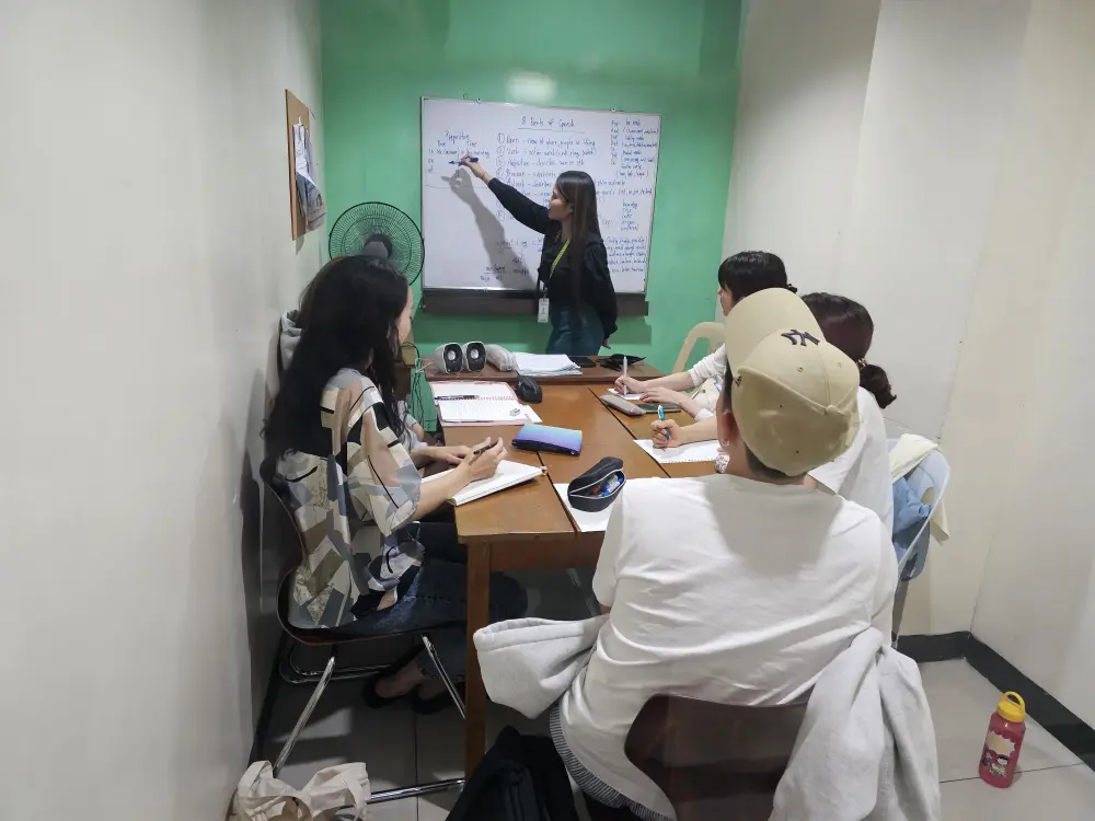 グループクラスでホワイトボードの前に立つ講師の説明に聞き入る5人の学生