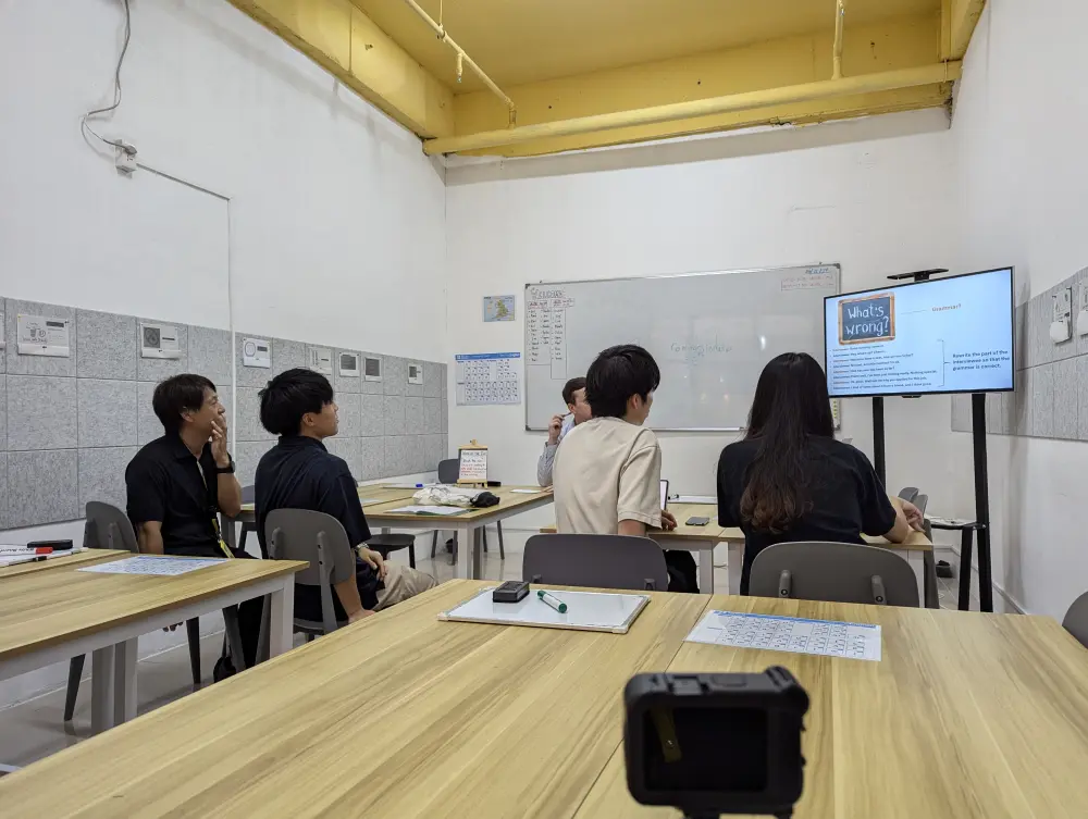 ネイティブ講師のグループクラスでモニターを真剣に見る3人の学生とGrit留学の真太郎