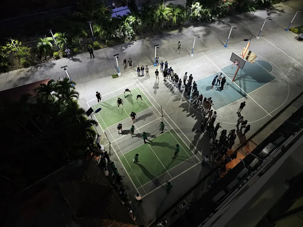 B’Cebuの校庭でバレーボールの試合を行っている各国の学生と周囲で観戦する学生たち