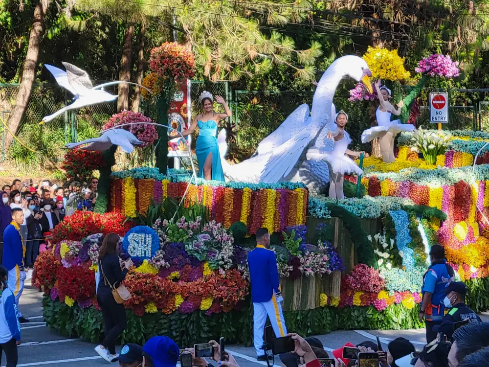 BaguioのPanagbenga Festivalの生花で飾り付けられた巨大な山車とそのうえでポーズをとる3人の女性