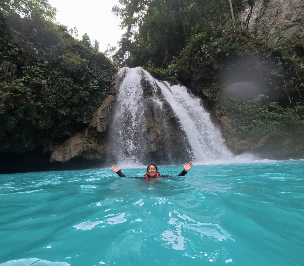 セブのカワサン滝のエメラルド色の水で泳ぎながら写真にポーズを取るGrit留学の真太郎