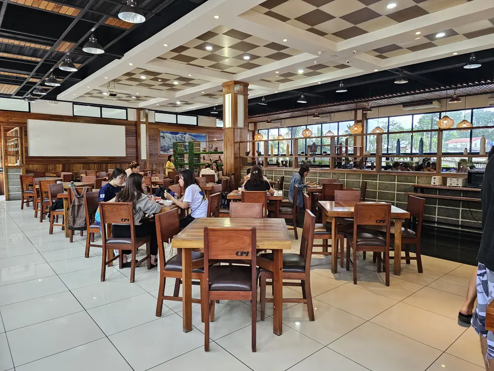 CPIのダイニングに並べられた複数の木製テーブルセットと昼食を楽しむ学生たち