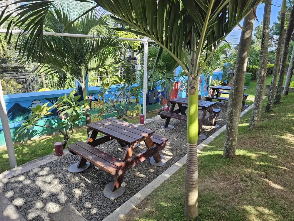 ヤシの木に囲まれ、木製のテーブルセットが3台並ぶ屋外喫煙エリア