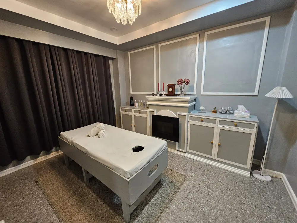 白とグレーを基調とした内装のマッサージルームと部屋の中央に配置された施術ベッド