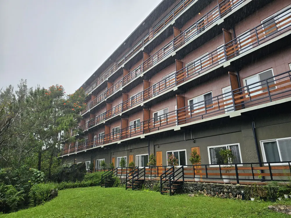 雨の日に撮影された山に面したJICプレミアムキャンパス学生寮の斜め正面外観