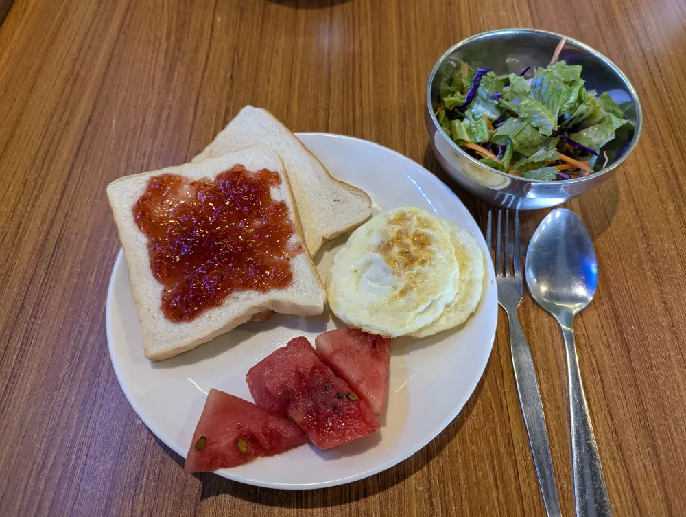 目玉焼き2つ、食パン2枚、スイカ4切れが盛られた朝食プレートとサラダボウル